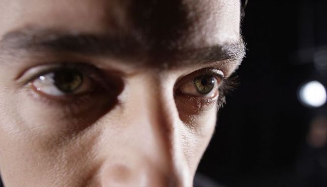 Intense closeup male gaze revealing eyes, eyelashes, pores and bridge in low-key light