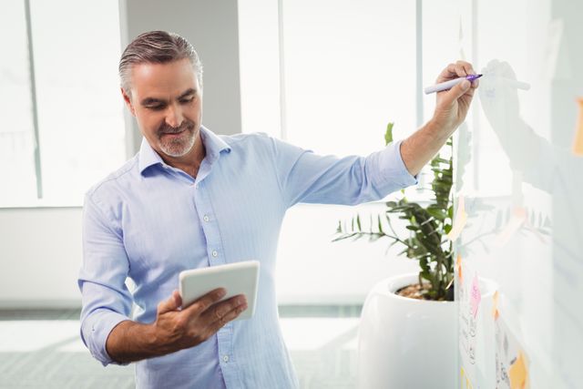 Attentive executive using digital tablet while writing on whiteboard in office