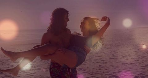 Man carrying laughing woman on beach at sunset during golden hour with lens flare romance