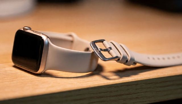 Silver smartwatch resting on wooden surface with cream silicone strap and metal buckle