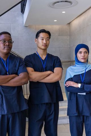 Diverse healthcare team standing with arms crossed in hospital corridor wearing navy scrubs