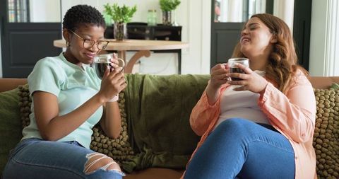 African american women sharing coffee and laughter on cozy green sofa