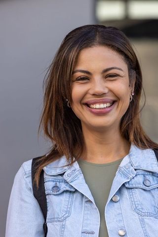 African american woman smiling on urban sidewalk wearing denim jacket and backpack