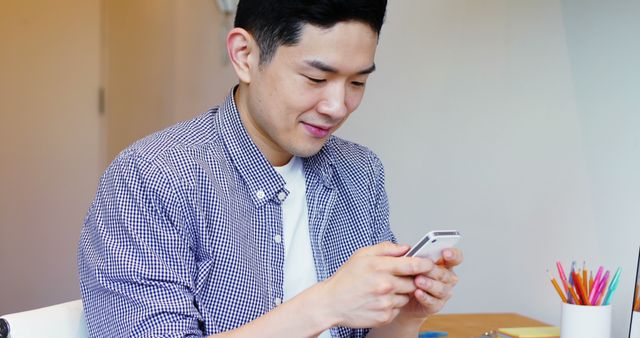 Young Man Smiling and Using Smartphone at Desk - Download Free Stock Images Pikwizard.com