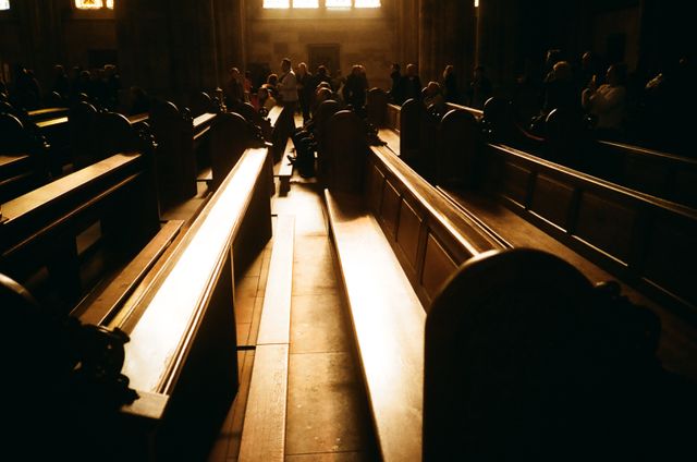 Church pews bathed in warm sunlight with gathered congregation throughout. Ideal for conveying themes of worship, faith, and spirituality. Suitable for content related to religious practices, sacred spaces, or architectural validation within places of worship.