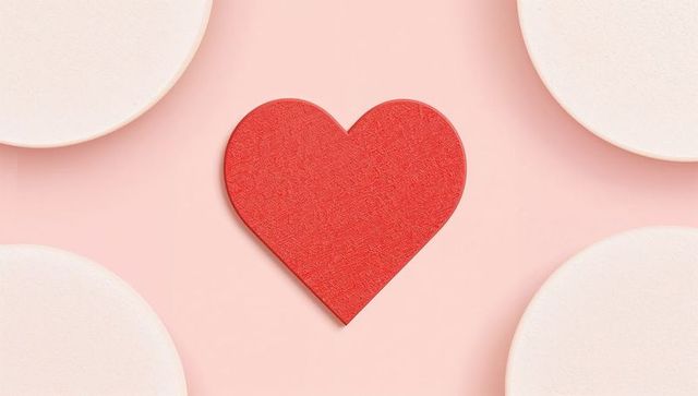 Red textured heart centered on pastel pink tabletop with cream circles minimal flatlay