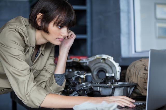 Female mechanic leaning on table and using laptop at the repair garage