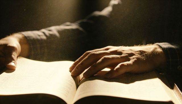 Hands resting and turning open book page in warm low light with dust motes