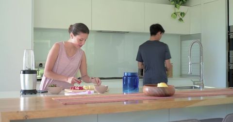 Couple preparing fresh fruit on wooden island in modern sunlit kitchen, home cooking