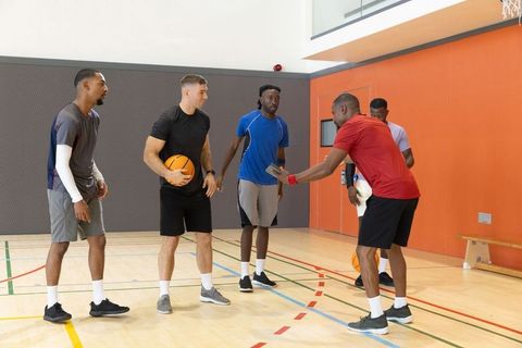 Diverse men playing basketball in indoor gym during team practice and coaching session