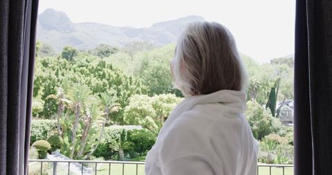Senior Woman in Bathrobe Enjoying Tranquil Garden View on Balcony