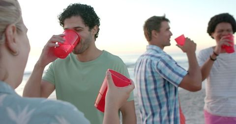 Friends Celebrating with Drinks by the Beach at Sunset