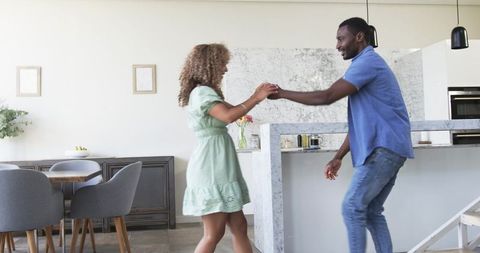 Diverse couple holding hands and dancing at marble kitchen island in modern home