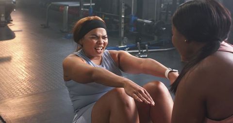 Diverse mid-adult women performing partner abdominal crunches with smartwatch in gym