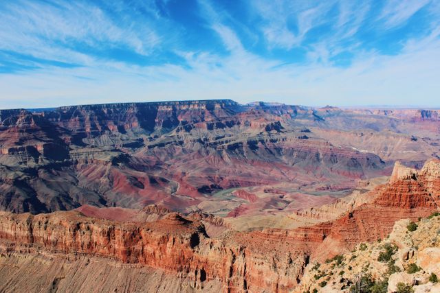 Stunning landscape showcasing the vast and rugged terrain of the Grand Canyon under a clear, bright blue sky. The unique geological formations and red rock cliffs make it a perfect fit for travel websites, nature documentaries, outdoor adventure blogs, and educational material about natural wonders.