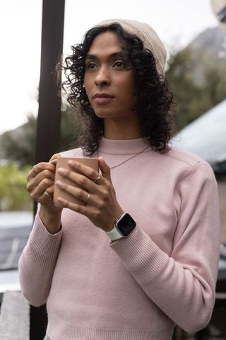 Young woman holding mug on balcony wearing pale pink sweater and beige beanie