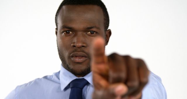 Close-up of an African man in a blue shirt and tie pointing his finger forward with a serious and assertive expression. Ideal for usage in business contexts, conveying messages about determination, leadership, or direction. This can also be a powerful visual for marketing campaigns, motivational materials, or articles focusing on personal development and success.