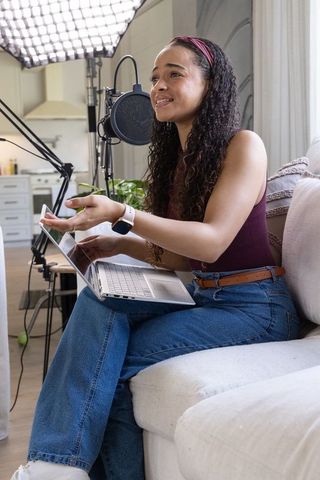 African american woman recording podcast at home studio with laptop and professional mic