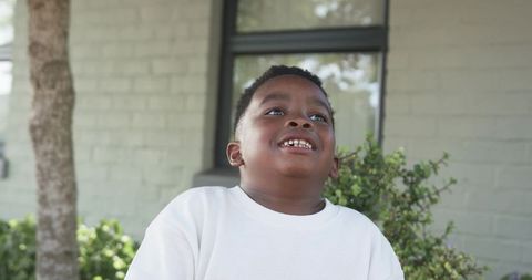 African American Boy Smiling and Looking Up Outdoors in White Shirt Urban Home Background