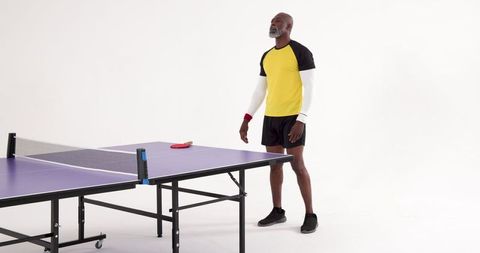 Man standing by table tennis table holding paddle in studio