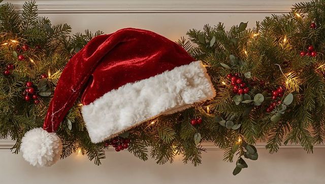 Resting red velvet Santa hat on garland with eucalyptus, berries and warm fairy lights