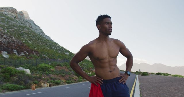African american man standing and flexing his muscles on a coastal road. fitness training and healthy outdoor lifestyle.