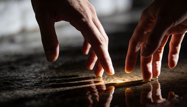 Hands tracing golden reflection on wet stone close-up, fingers hovering over mirror water