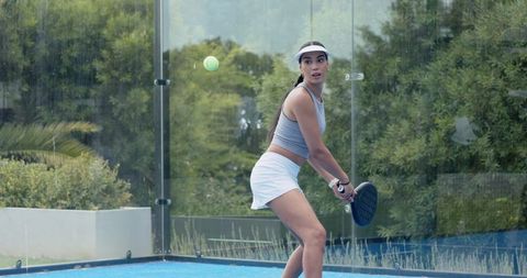 African american woman playing padel on blue court with glass wall outdoor athletic action