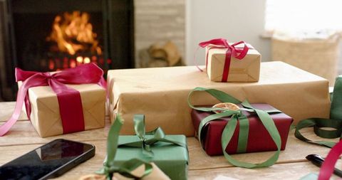 Cozy holiday gift table with wrapped presents, satin ribbons and warm fireplace glow