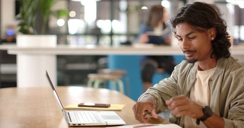 Young man studying with laptop and papers on wooden table in modern coworking space