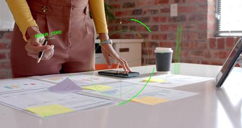 Designer leaning over studio desk reviewing wireframes and mobile prototype with coffee
