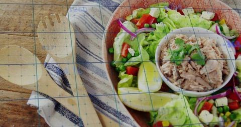 Rustic tuna salad bowl serving with lemon wedges, mixed greens, avocado and wooden spoons