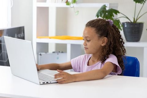 Young girl using laptop in bright tidy workspace at home for online learning and studying