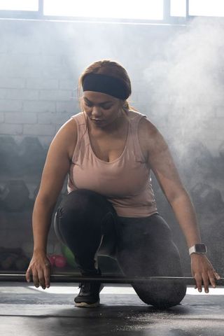 African american woman preparing barbell for powerlifting in gym with chalk dust and rimlight