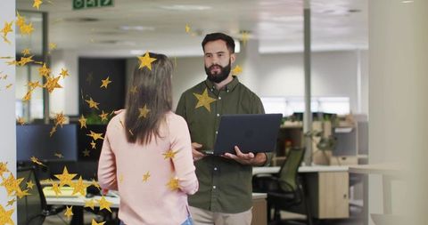 Bearded man holding laptop explaining project to colleague with gold stars in modern office