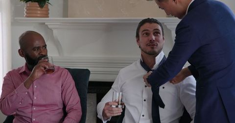 Groom receiving help with tie from friend before wedding