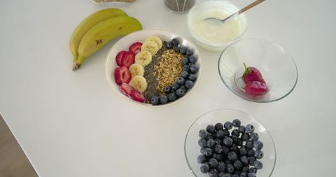 Colorful breakfast bowl with granola, chia seeds, bananas and berries on white countertop
