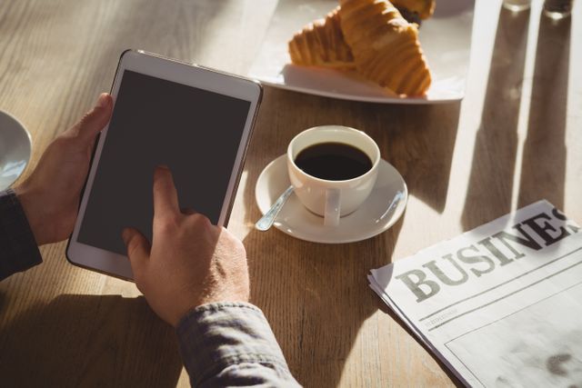 Cropped hands of businessman using digital tablet by coffee cup at table in cafe