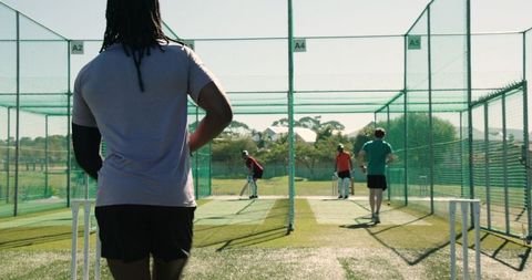 Multiracial teammates practicing bowling drills in outdoor cricket nets during team training