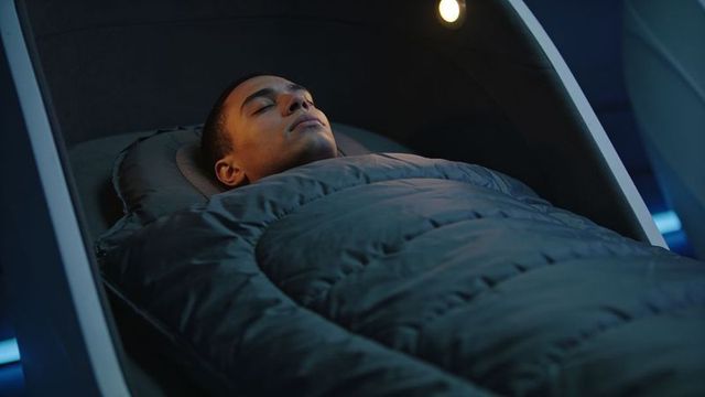 Adult male resting in futuristic sleep pod with quilted cocoon and ambient blue lighting