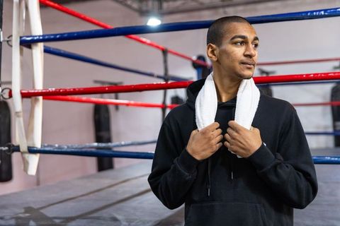 Young asian boxer standing by ring holding towel after intense training session