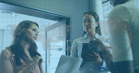 Women collaborating over digital world map on office glass wall during data-driven meeting