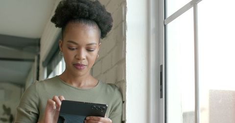 African American Businesswoman Engaging with Smartphone Near Window