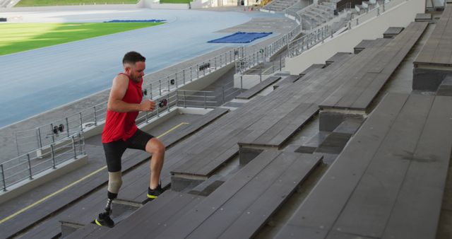 Image capturing a determined athlete with a prosthetic leg running up the stairs in a large stadium. Ideal for content related to fitness, sports, motivation, perseverance, and overcoming obstacles. Can be used in websites, magazines, and advertisements promoting an active lifestyle and inspirational stories.