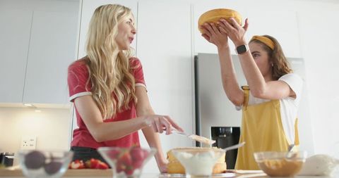 Two women stacking and frosting cake on bright kitchen island with fresh strawberries