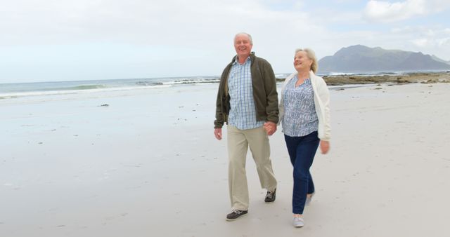 Happy senior caucasian couple holding hands and walking on beach, copy space. Retirement, summer, leisure, vacation and senior lifestyle, unaltered.