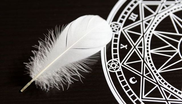 White feather resting on dark wood beside intricate geometric mandala for spiritual design