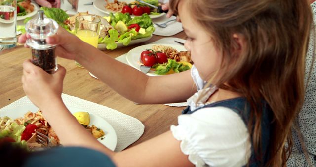 Young girl seasoning meal during family dinner - Download Free Stock Images Pikwizard.com