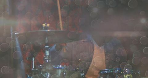 Denim-clad drummer playing drums in artistic room with floating bokeh