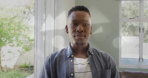 Young man standing by sliding glass door looking at camera in bright modern living room